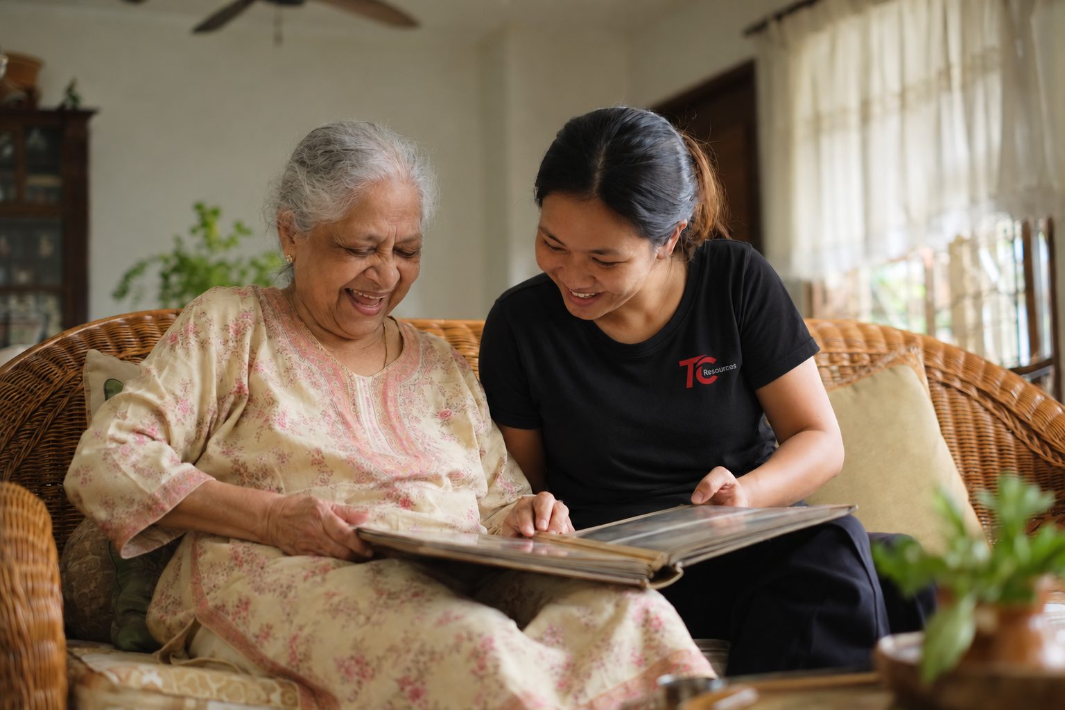 An elderly woman and her helper laughing over an old photo album